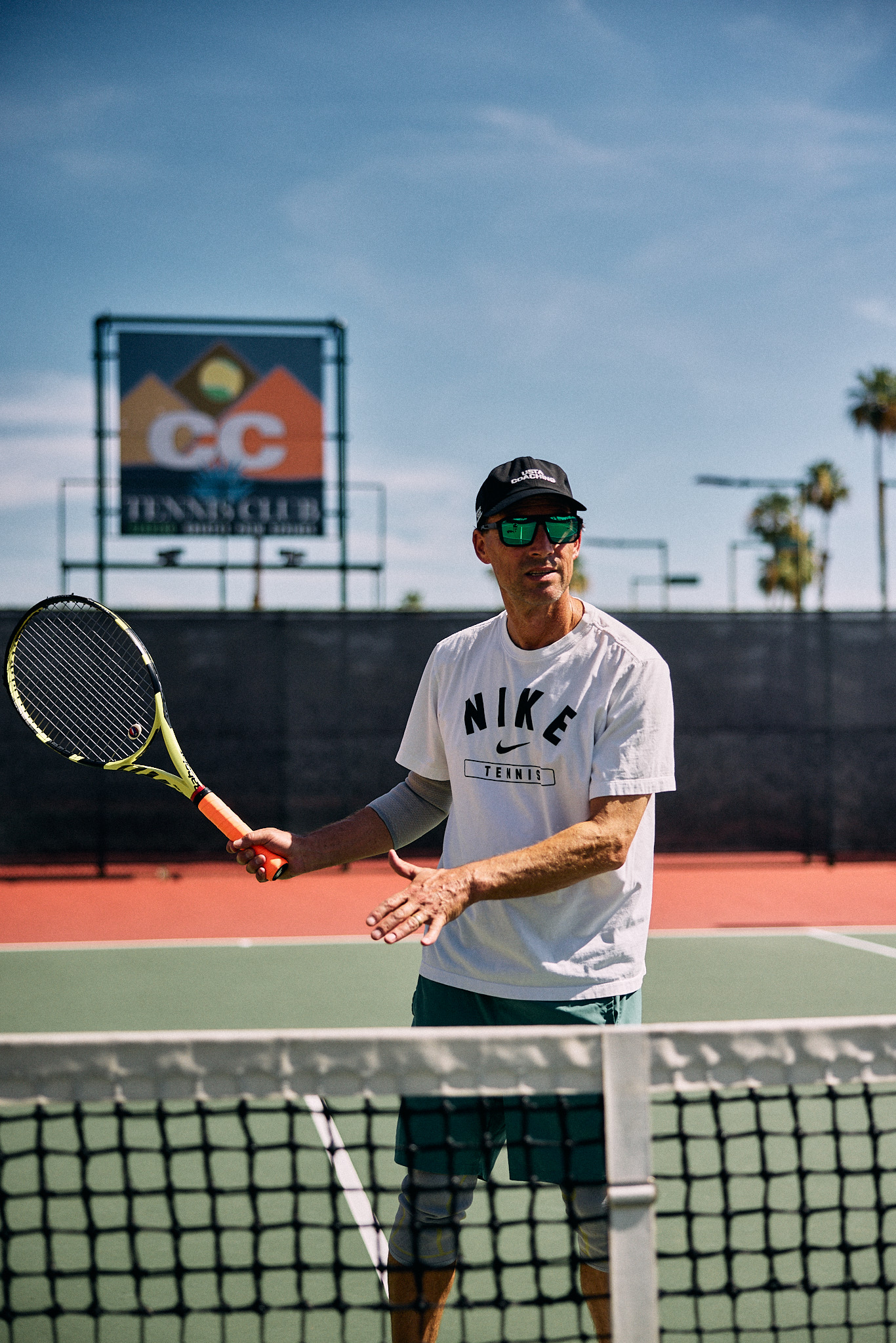 Coach Nathan Chesbro on court mid-lesson, racket in hand, demonstrating a stroke.
